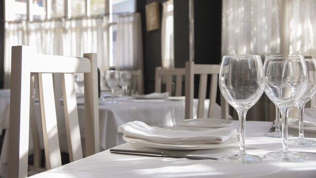 A dining table set with plates, a knife, and wine glasses, with a view of the outside through large windows. - Hotel Los Bartolos (Alhama de Murcia)