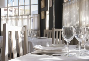 A dining table set with plates, a knife, and wine glasses, with a view of the outside through large windows. - Hotel Los Bartolos (Alhama de Murcia)