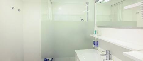 Un baño moderno con cabina de ducha de vidrio, un lavabo blanco y un espejo sobre él.