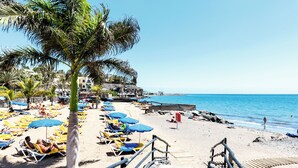 A beach with sun loungers and umbrellas, a wooden staircase leading down to the beach, and a clear blue sky. - Grupotel Tres Vidas (San Bartolomé de Tirajana)