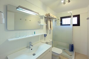 Un baño moderno con un espejo grande, un lavabo, un inodoro y una ducha con mampara de vidrio.