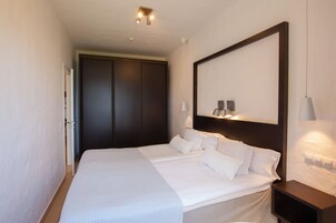 A hotel room with a large bed, a dark wardrobe, and a nightstand with a lamp.