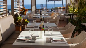 A restaurant with tables set for dining, a view of the ocean, and outdoor seating with plants. - Grupotel Tres Vidas (San Bartolomé de Tirajana)