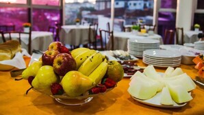 A table with a fruit bowl containing pears, apples, bananas, and strawberries, and a plate with sliced melon. - Hotel Saint Martin (Bauru)