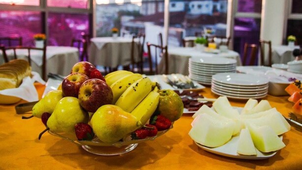 Une table sur laquelle se trouve un panier de fruits contenant des poires, des pommes, des bananes et des fraises, ainsi qu’une assiette de melon coupé en tranches.