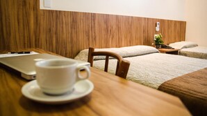 Une chambre d’hôtel avec une tête de lit en bois, un lit recouvert d’une couvre-lit à motifs, une table de chevet ornée d’une plante et un ordinateur portable posé sur le bureau.