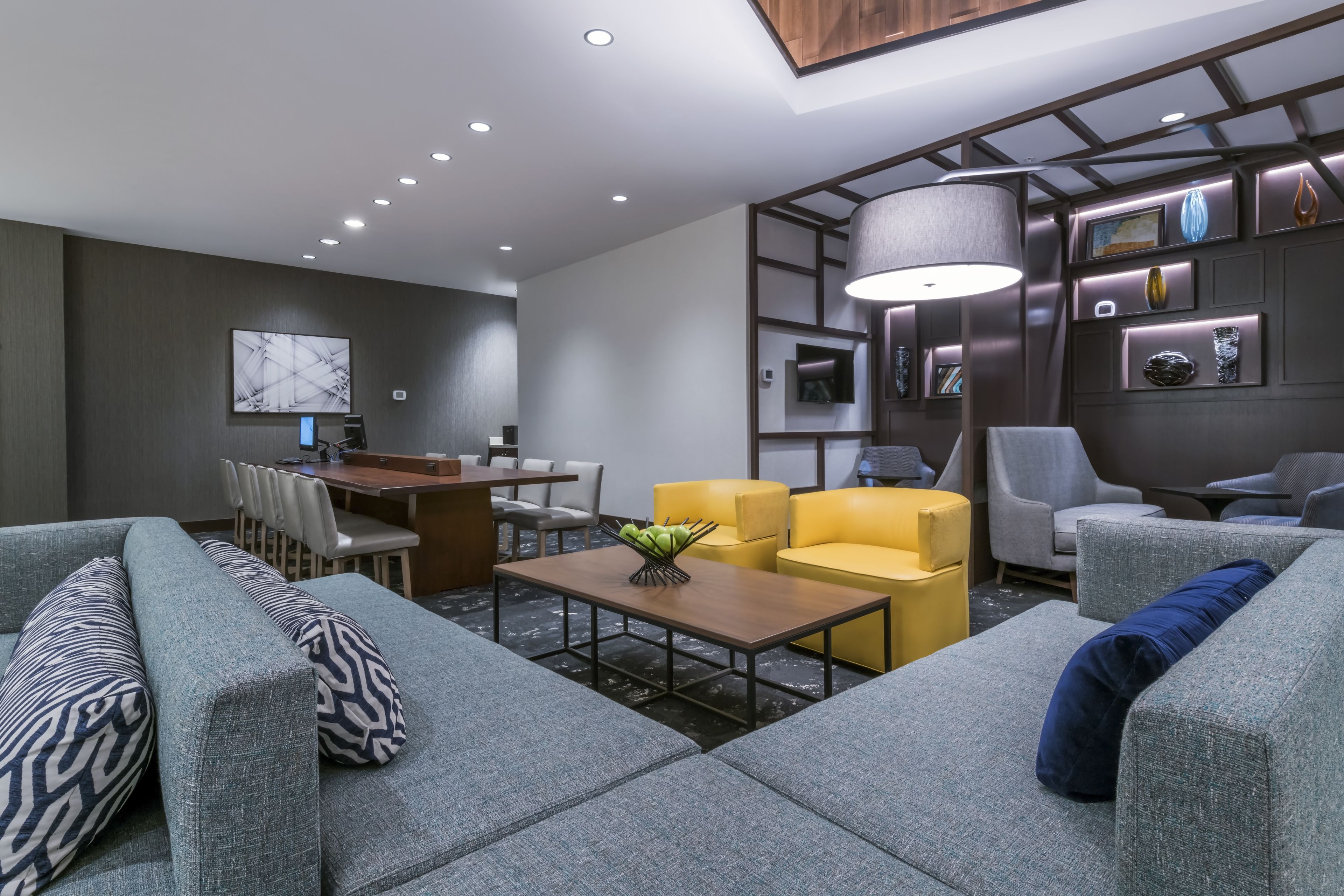 Un hall d’hôtel moderne avec des canapés gris, une table basse en bois et un coin repas comprenant des chaises et une table.