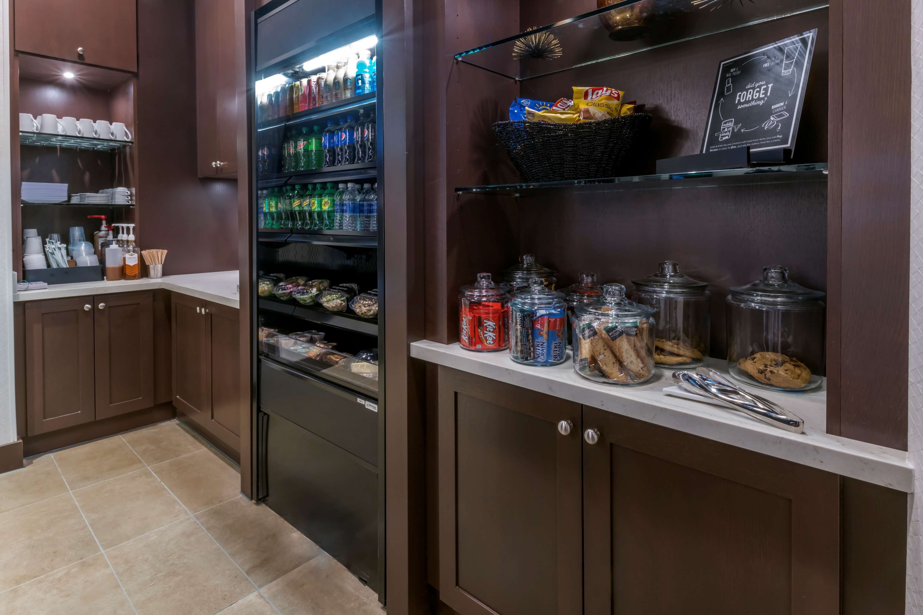 Un coin cuisine équipé d’un réfrigérateur rempli de boissons, d’une étagère avec des en-cas et de pots contenant des condiments.