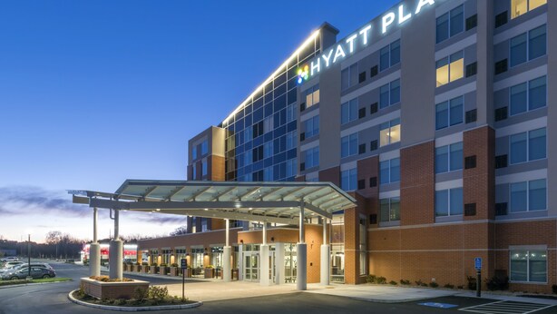 Un hotel de varios pisos con un llamativo letrero de "Hyatt Place", un acceso cubierto y un estacionamiento.