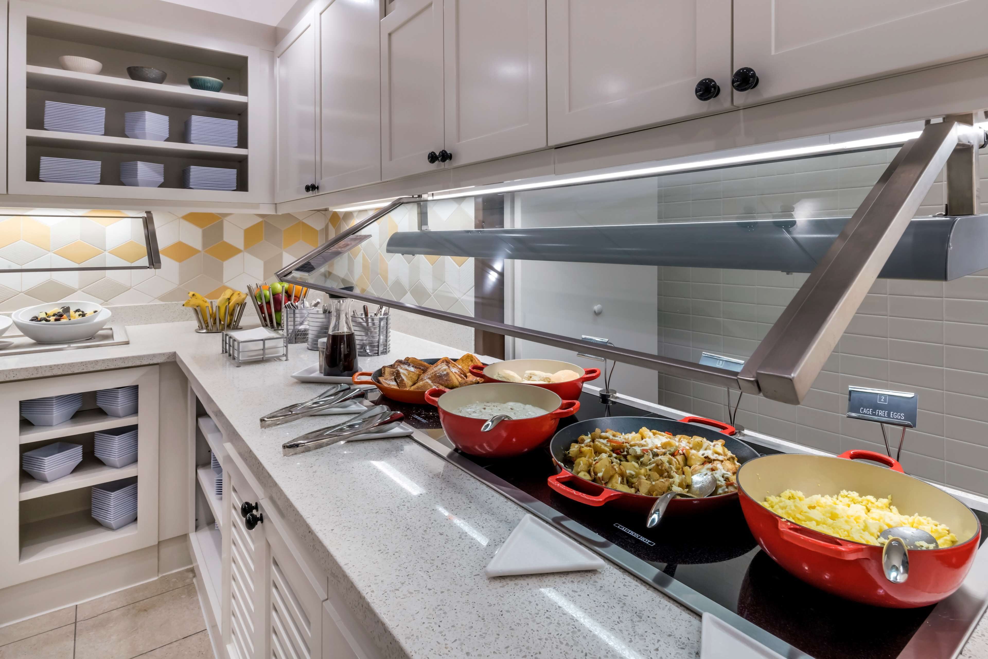 A buffet setup with various dishes, including a red pot of soup and a bowl of scrambled eggs.