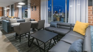 Un área de estar moderna con sofás y sillones de cuero, y una mesa de centro. Ventanas amplias ofrecen vistas a la ciudad.