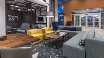 A modern lobby with seating areas, a wooden reception desk, and a large window with an exit sign.