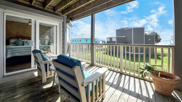 A covered outdoor area with a wooden deck, a sofa, and a potted plant. - OCEAN WAVES HEARD FROM 2 BALCONIES! 2 min walk to Beach;3 Baths, WIFI, 3 baths (Jamaica Beach)