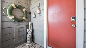 A red door with a keypad lock, a green lifebuoy, and a small wooden figure on a porch. - OCEAN WAVES HEARD FROM 2 BALCONIES! 2 min walk to Beach;3 Baths, WIFI, 3 baths (Jamaica Beach)