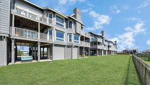 A multi-story residential building with balconies, a grassy lawn, and a wooden fence. - OCEAN WAVES HEARD FROM 2 BALCONIES! 2 min walk to Beach;3 Baths, WIFI, 3 baths (Jamaica Beach)
