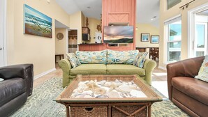 A living room with a green sofa, a brown leather sofa, and a glass coffee table with seashells. - OCEAN WAVES HEARD FROM 2 BALCONIES! 2 min walk to Beach;3 Baths, WIFI, 3 baths (Jamaica Beach)