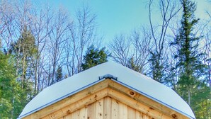 Een houten chalet met een met sneeuw bedekte dak, een witte deur en een klein terras.