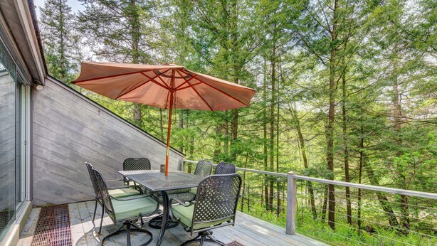 Een terras met een tafel, stoelen, een parasol en uitzicht op een bos.