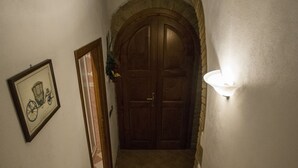 Un pasillo con una puerta de madera al final, un cuadro en la pared y una lámpara fijada a la pared.