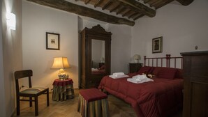 Un dormitorio con una cama de madera, una silla, una mesita de noche con lámpara, un espejo y una pequeña mesa con lámpara.