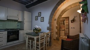 Una cocina con armarios blancos, una mesa de comedor con sillas, un jarrón de flores y un arco de ladrillo que conduce a un baño.