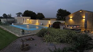 Un jardin avec une piscine, un espace salon extérieur et une structure en bois illuminée.