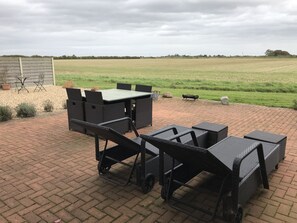 Une terrasse extérieure avec un sol en briques, des meubles en osier noir et une vue sur un champ verdoyant.