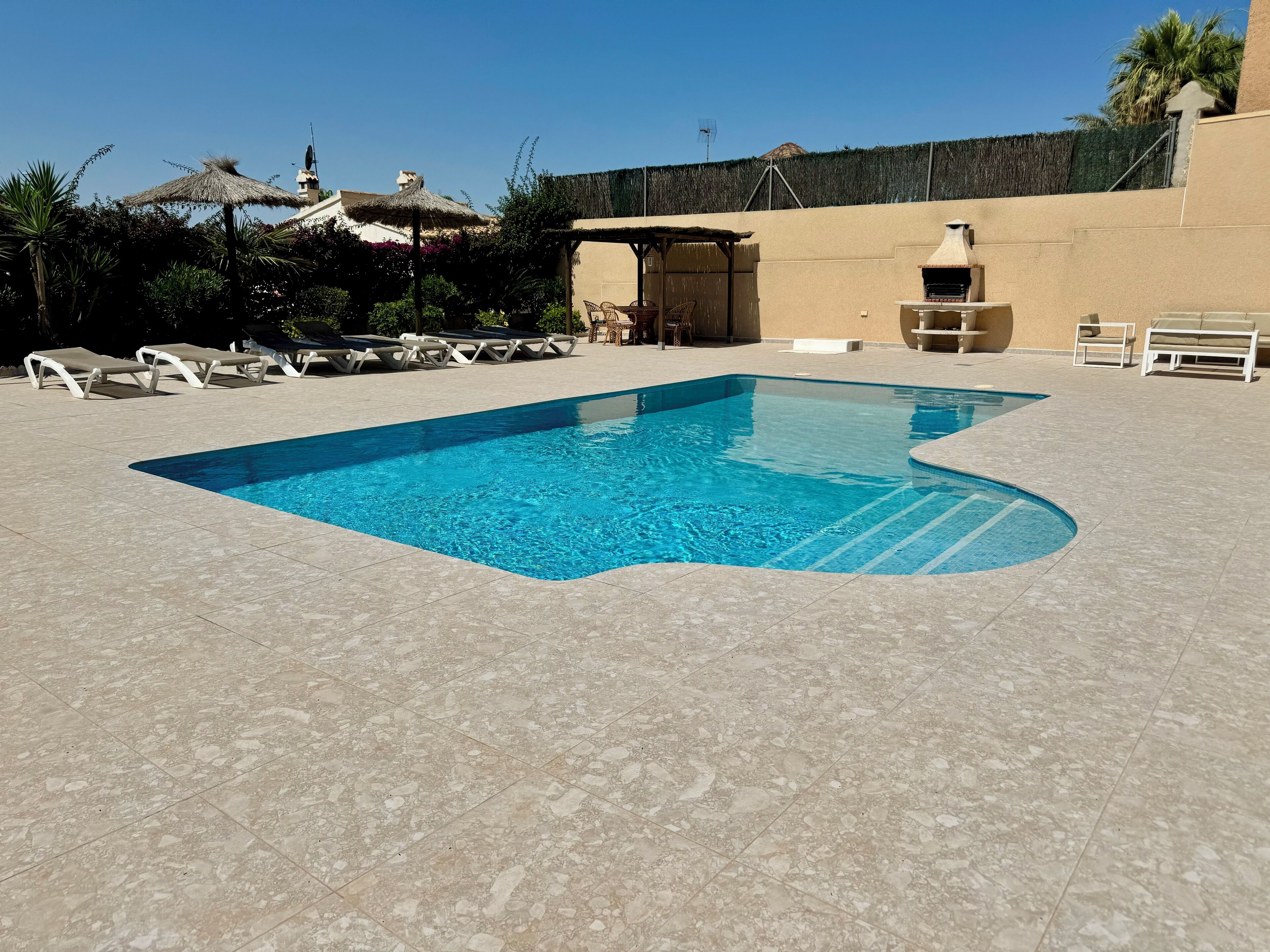 Une piscine avec des chaises longues et un espace barbecue.