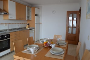 Une cuisine moderne avec des meubles en bois, un réfrigérateur et une table à manger mise pour deux personnes, avec des assiettes, des tasses et des couverts.