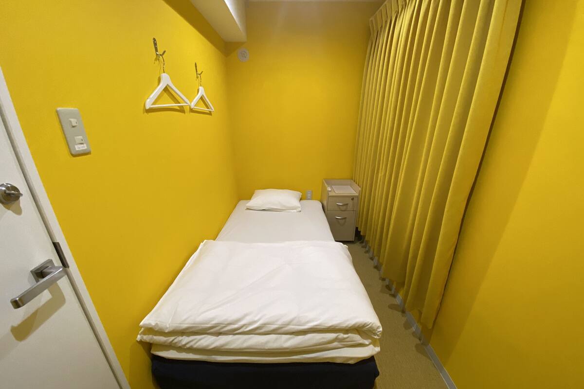Um quarto pequeno e colorido, com uma cama, um criado-mudo e um interruptor de luz fixado na parede.
