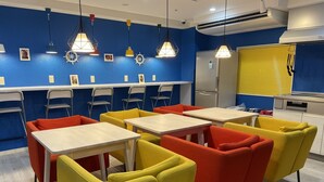 Un comedor con mesas y sillas, una zona de cocina con electrodomésticos, y una pared azul con adornos.