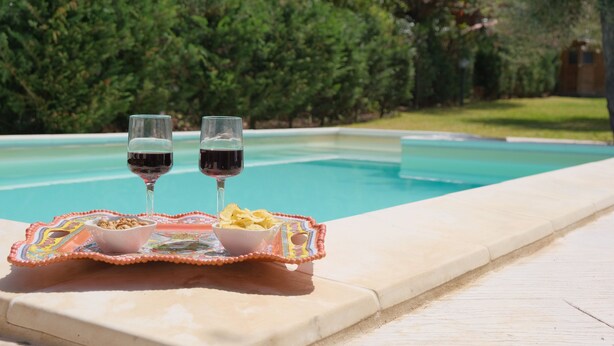 A poolside setting with two glasses of red wine and snacks on a tray. - Villa of Wings (Capo)