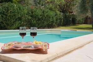 A poolside setting with two glasses of red wine and snacks on a tray. - Villa of Wings (Capo)