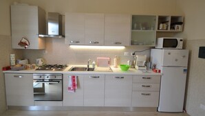 A compact kitchen with white cabinets, a gas stove, a sink, a microwave, and a refrigerator.