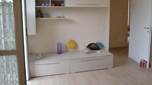 A room with a built-in wardrobe, a small shelf with decorative items, and a door leading to another room.