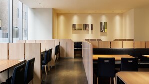 Een modern restaurant met hoge tafels en zitjes, houten scheidingswanden en uitzicht op de stad door grote ramen.