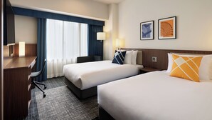 Een hotelkamer met twee bedden, een bureau, een stoel en een televisie.