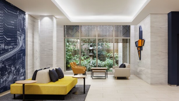Een moderne woonkamer met een gele bank, een beige bank en een houten bankje. Er is een groot raam met uitzicht op groen en een pagode.