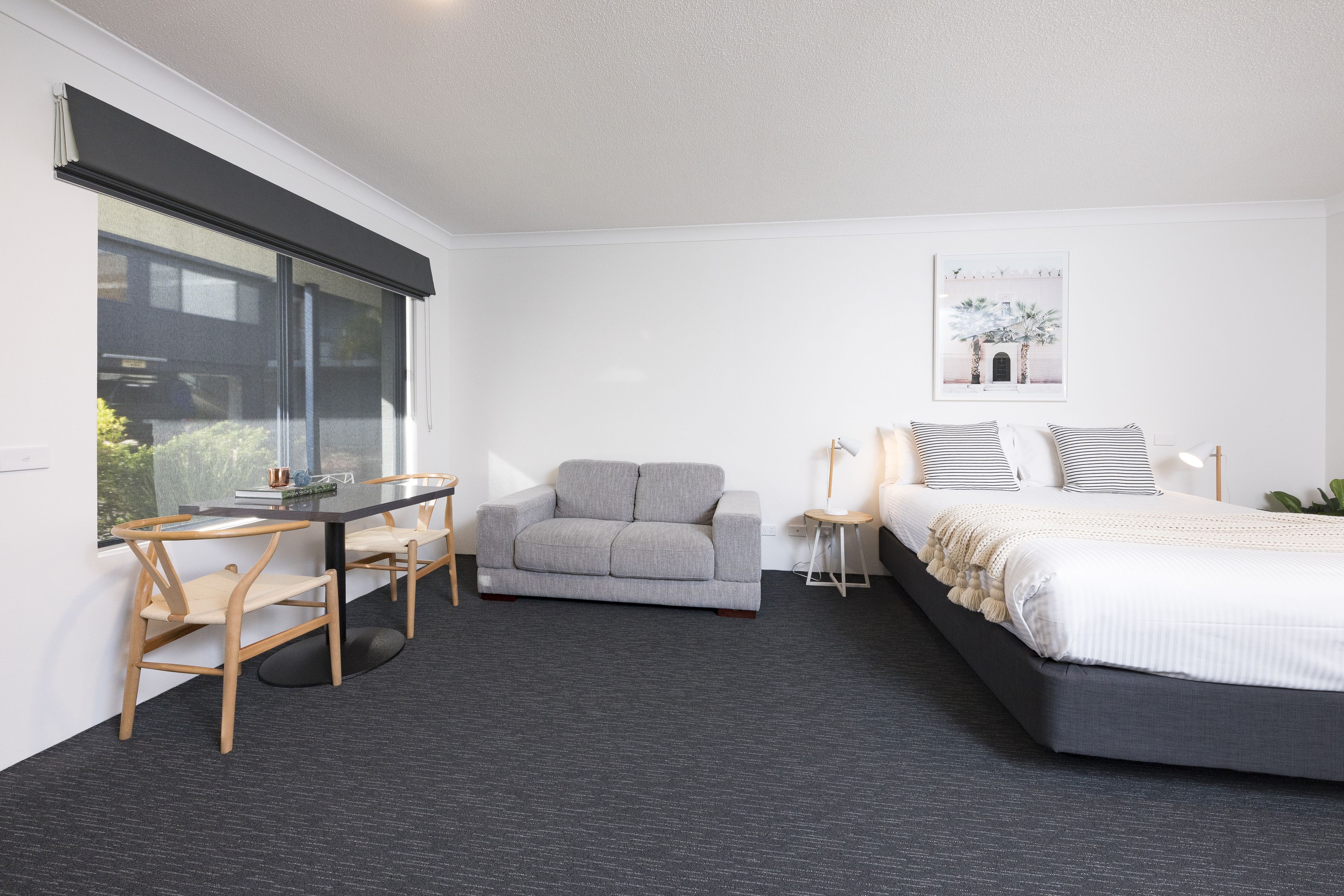 Una habitación de hotel moderna con una cama grande, un sofá gris, una mesita pequeña y un escritorio.