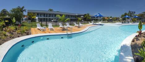 A swimming pool with lounge chairs and umbrellas, surrounded by a fence and palm trees.