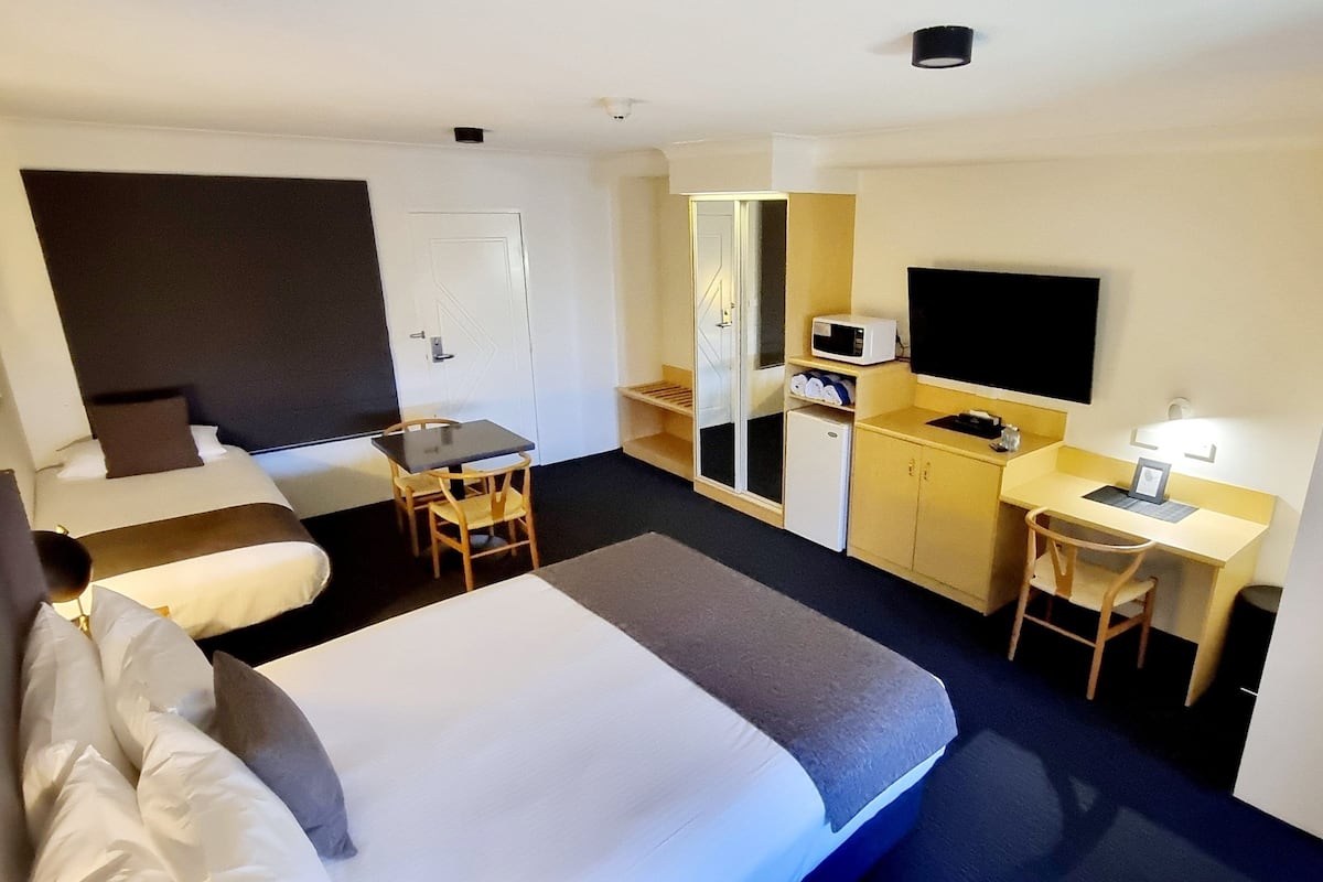 Habitación de hotel con cama, escritorio, silla, televisor, microondas y armario.