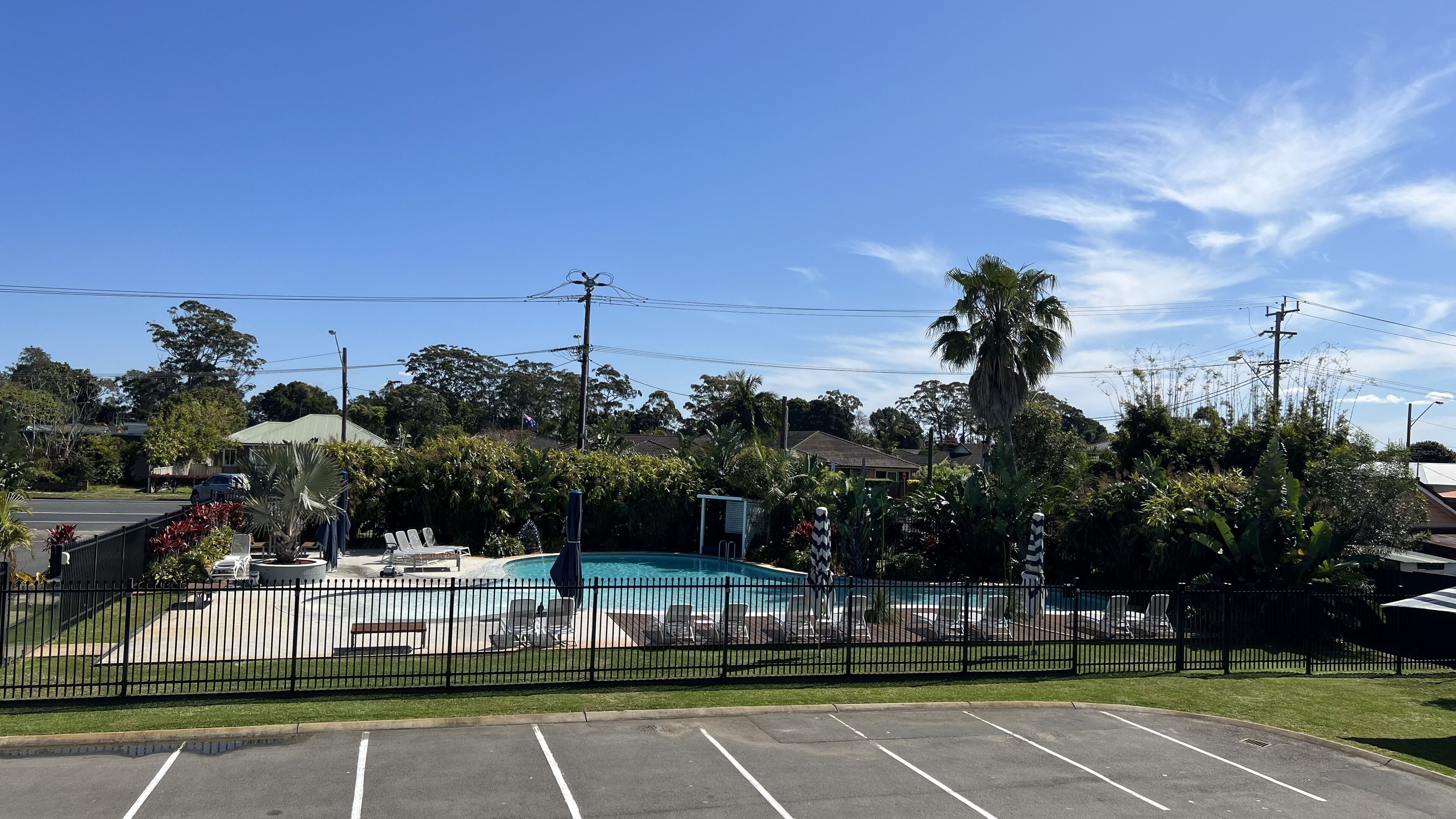 Une piscine entourée d’une clôture, avec des chaises longues et un petit bâtiment en arrière-plan.