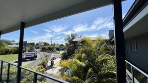 Varanda com vista para uma rua residencial, uma caminhonete de entregas estacionada e vegetação exuberante.