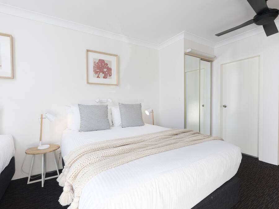 A modern hotel room with a large bed, a bedside table with a lamp, and a ceiling fan.