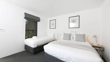 A hotel room with two beds, a large window with a blackout blind, two framed artworks on the wall, and a bedside table with a lamp.