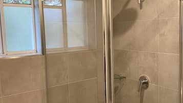 Une salle de bain avec une douche à parois de verre, des toilettes et une fenêtre.