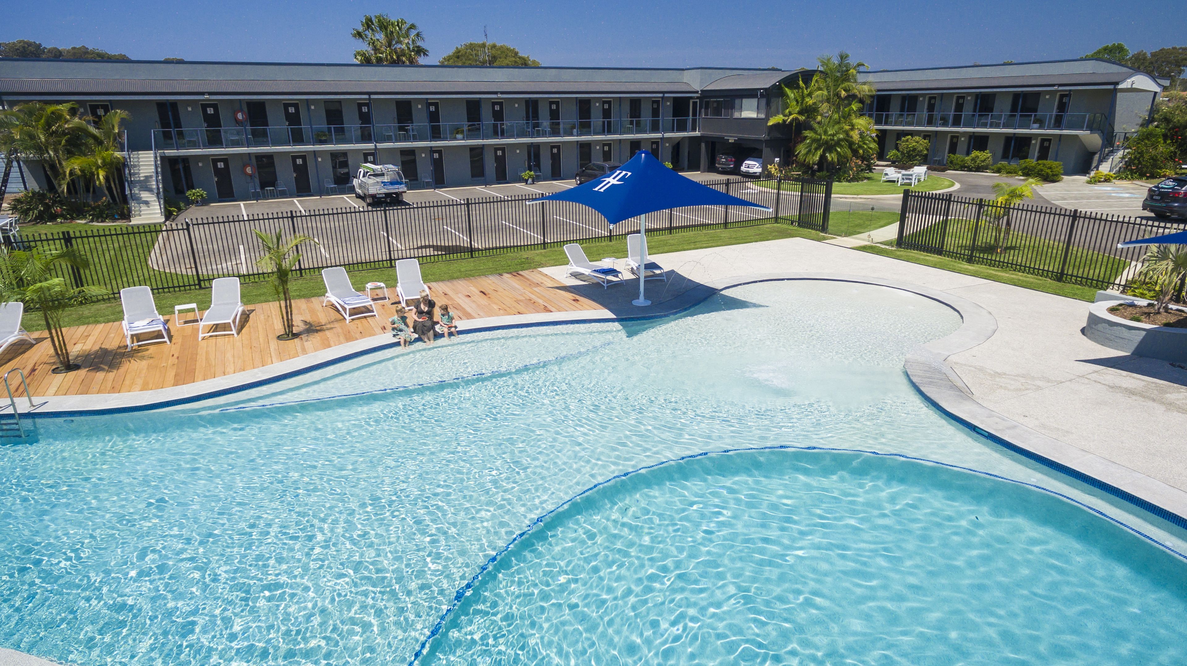 A swimming pool with a wooden deck, lounge chairs, and a blue canopy.