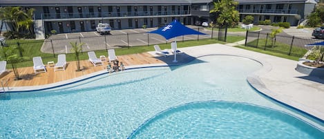 A swimming pool with a wooden deck, lounge chairs, and a blue canopy.