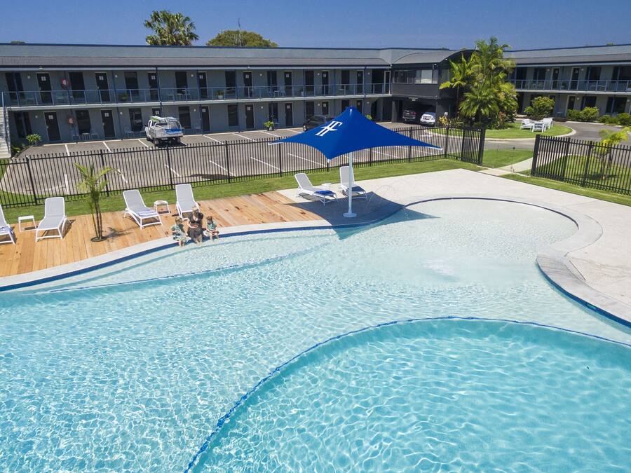 A swimming pool with a wooden deck, lounge chairs, and a blue canopy.