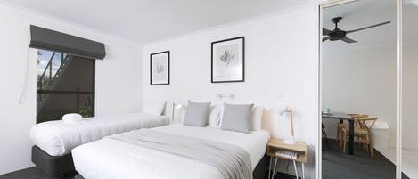 A modern hotel room with two beds, a desk, a chair, a mirror, and a ceiling fan.